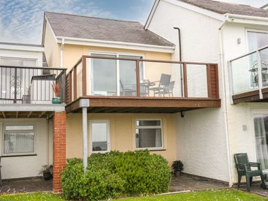 Exterior view of a two-story house with a balcony that has glass panels and outdoor furniture at Delfryd in Y Felinheli