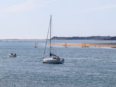 A body of water with sailboats and a motorboat near a sandy shore with people on the beach at Delfryd in Y Felinheli
