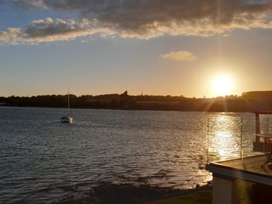 A body of water with a sailboat and a setting sun with a deck railing at Delfryd in Y Felinheli