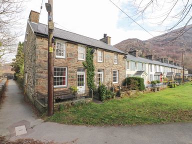 A row of stone and painted terraced houses with small front gardens and a grassy area in front at Brackenbury Cottage in Beddgelert