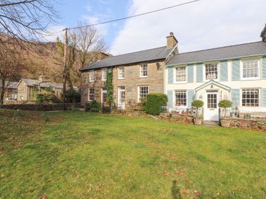 Stone and painted houses with windows and doors facing a lawn with scattered leaves and trees in the background at Brackenbury Cottage in Beddgelert