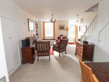 A living room with two chairs a fireplace a wooden sideboard and stairs at Brackenbury Cottage in Beddgelert