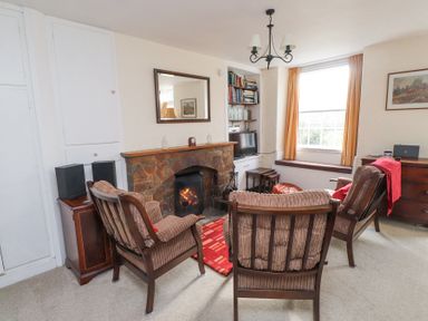 A living room with a fireplace two armchairs TV and a window with yellow curtains at Brackenbury Cottage in Beddgelert