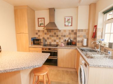 A kitchen with light wood cabinets a stove microwave kettle sink and washing machine at Brackenbury Cottage in Beddgelert