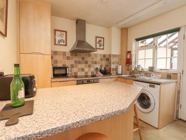 A kitchen with granite countertops a washing machine toaster microwave and a window at Brackenbury Cottage in Beddgelert