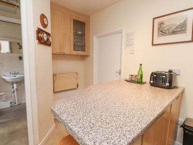 A kitchen counter with a toaster bottle and cup next to a door and a cabinet with glassware at Brackenbury Cottage in Beddgelert