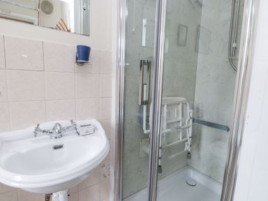 A bathroom with a white sink and a shower area with a foldable shower seat at Brackenbury Cottage in Beddgelert