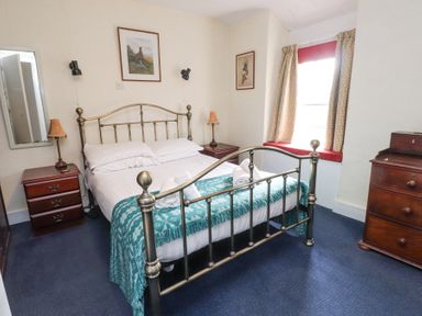 A bedroom with a metal bed frame bedside tables lamps dresser and a window with curtains at Brackenbury Cottage in Beddgelert