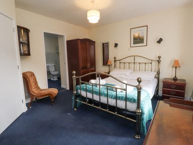 A bedroom with a metal bed frame a wooden wardrobe an orange chair and an ensuite bathroom at Brackenbury Cottage in Beddgelert