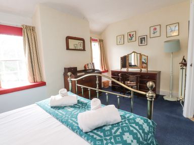 A bedroom with a brass bed frame towels on bed a wooden desk with mirror and chair a floor lamp and framed pictures on the wall at Brackenbury Cottage in Beddgelert