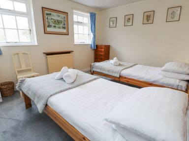 A bedroom with two single beds with blankets and rolled towels two windows a chair a chest of drawers and framed pictures on the walls at Brackenbury Cottage in Beddgelert