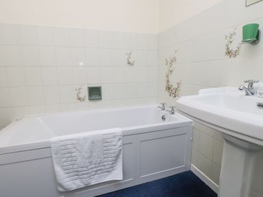 A bathroom with a bathtub a towel on the bathtub and a sink with a green cup at Brackenbury Cottage in Beddgelert