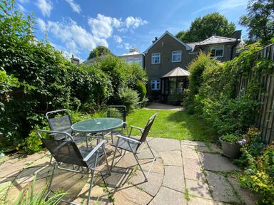 A garden with a glass table and four chairs on a stone patio at Brackenbury Cottage in Beddgelert