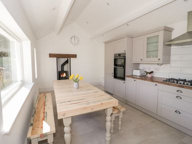 A kitchen with a wooden table and bench seating a wood stove and modern kitchen cabinets at Y Gogarth in Benllech