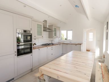 A kitchen with built in oven hob range hood wooden countertops and a wooden dining table with benches at Y Gogarth in Benllech