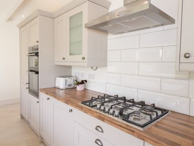 A kitchen with wooden countertops a gas stove a white toaster and white cabinets at Y Gogarth in Benllech