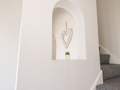 A white alcove with a heart decoration and a small potted plant next to carpeted stairs at Y Gogarth in Benllech