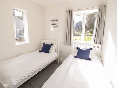 A bedroom with two single beds each with a blue pillow and white bedding at Y Gogarth in Benllech