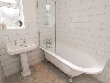 A bathroom with a pedestal sink and clawfoot bathtub with shower at Y Gogarth in Benllech