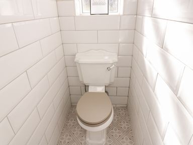 A small bathroom with a toilet centered between white tiled walls and patterned tiled floor at Y Gogarth in Benllech