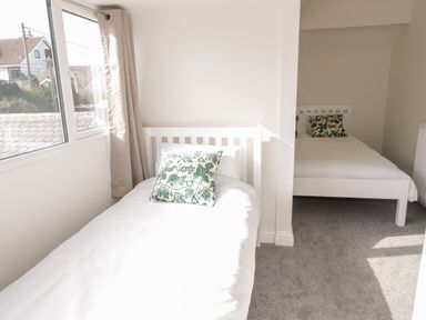 A bedroom with two white beds and patterned pillows near a window at Y Gogarth in Benllech