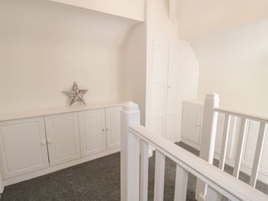 A hallway with built-in cabinets a metal star decoration and white railing at Y Gogarth in Benllech