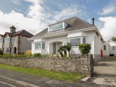 A white detached house with a stone wall and driveway at Y Gogarth in Benllech