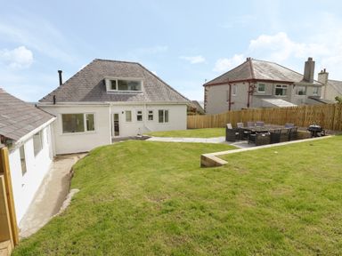 A backyard with a lawn and patio furniture near a white house at Y Gogarth in Benllech