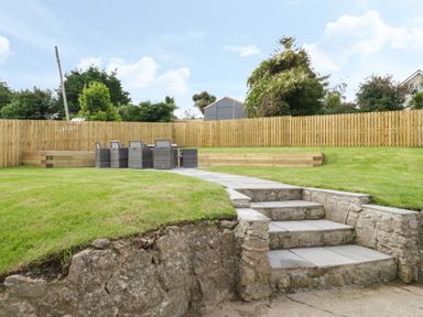 A backyard with stone steps leading to a patio area with chairs and a table at Y Gogarth in Benllech