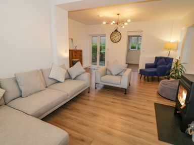A living room with beige sofas a blue armchair a wood stove and wooden flooring at Y Gogarth in Benllech