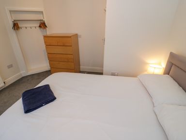 A bedroom with a bed and pillows a chest of drawers and an open closet with hangers at Y Gogarth in Benllech