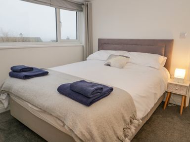 A bedroom with a bed with white sheets and two blue towels on a beige blanket at Y Gogarth in Benllech