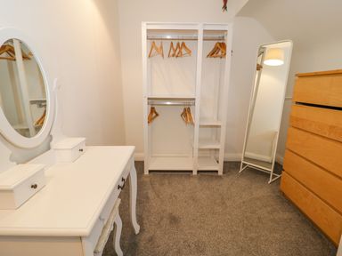 A dressing room with a white vanity table with mirror wooden hangers on a white open wardrobe a full length mirror and a wooden chest of drawers at Y Gogarth in Benllech