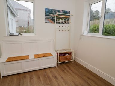 A corner of a room with a white bench with wooden seat panels a coat rack with a wicker basket and two windows at Y Gogarth in Benllech