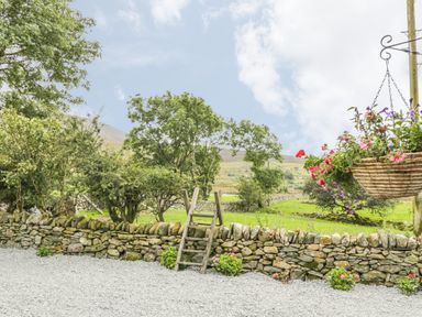 A stone wall with a wooden ladder and hanging flower basket overlooking a green field at Marchlyn in Deiniolen