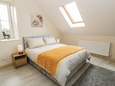 A bedroom with a double bed covered in yellow and gray bedding a wooden nightstand with a lamp a window a skylight and a gray rug at Marchlyn in Deiniolen