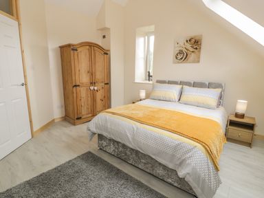 A bedroom with a double bed a wooden wardrobe two bedside tables with lamps and a gray rug at Marchlyn in Deiniolen