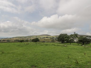 A green field with scattered trees and houses in the distance under a cloudy sky at Marchlyn in Deiniolen