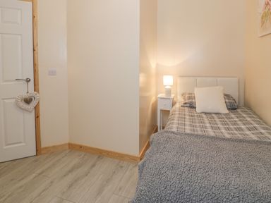 A small bedroom with a single bed with plaid bedding and a white bedside table with a lamp at Marchlyn in Deiniolen