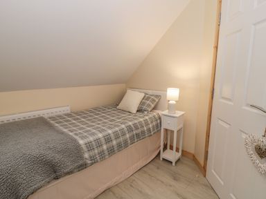 A small bedroom with a single bed a bedside table with a lamp and a door slightly open at Marchlyn in Deiniolen