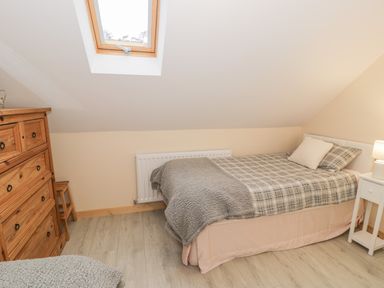 A bedroom with a single bed beside a white nightstand and a wooden chest of drawers under a skylight window at Marchlyn in Deiniolen