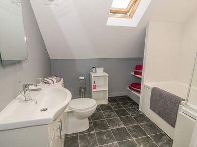 A bathroom with a sink toilet bathtub and shelves with towels at Marchlyn in Deiniolen
