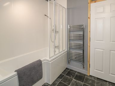 A bathroom with a bathtub shower combination towel rail and a white door at Marchlyn in Deiniolen