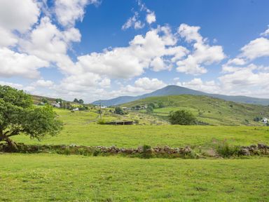 A green countryside landscape with hills trees and stone walls under a blue sky at Marchlyn in Deiniolen
