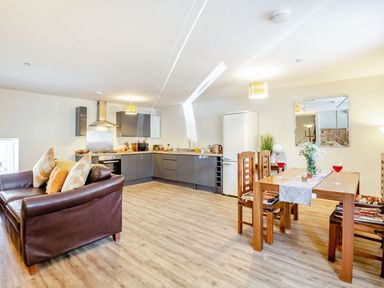 An open plan kitchen and dining area with a brown leather sofa a wooden dining table with chairs and a kitchen with grey cabinets at Marchlyn in Deiniolen
