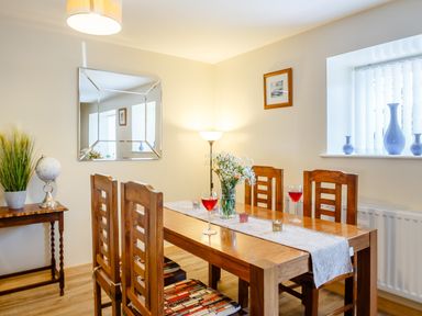 A dining room with a wooden table and four chairs with glasses of red liquid and a flower vase at Marchlyn in Deiniolen