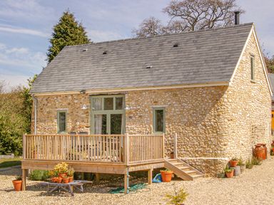 A stone house with a wooden deck and potted plants outside at The Apple Barn at Wyke Farm in Lyme Regis
