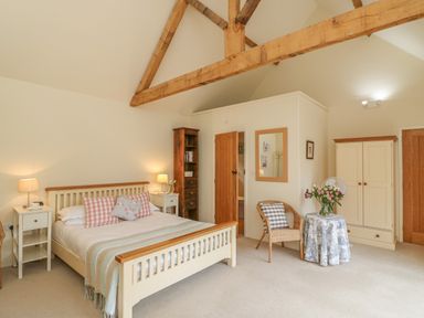 A bedroom with a double bed two bedside tables a wicker chair a small round table a wardrobe and exposed wooden beams at The Apple Barn at Wyke Farm in Lyme Regis