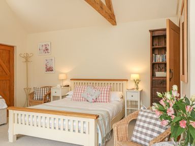 A bedroom with a large bed with pillows two wicker chairs bedside tables and lamps and a bookshelf at The Apple Barn at Wyke Farm in Lyme Regis