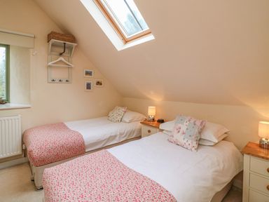 A bedroom with two single beds bedside tables lamps a skylight window and framed pictures on the wall at The Apple Barn at Wyke Farm in Lyme Regis